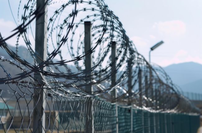 Barbed wire running along a wire fence with blue sky in the background